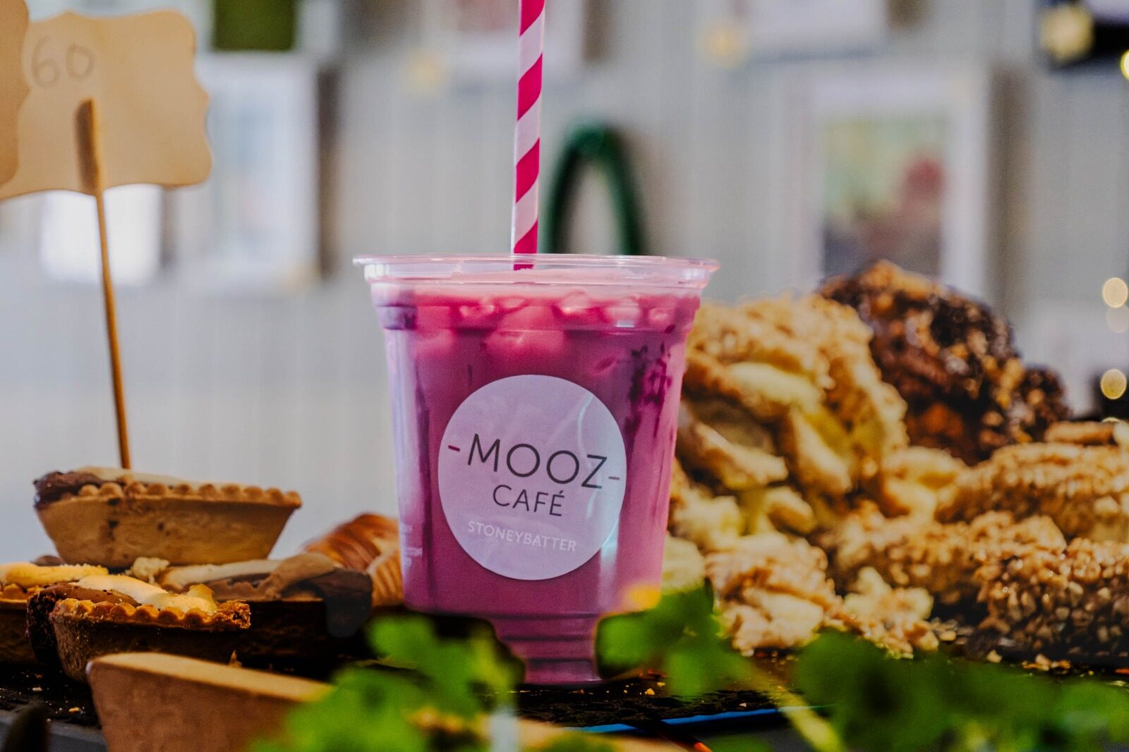 An iced pink drink in a Mooz Café Stoneybatter cup, surrounded by tarts and pastries on the counter